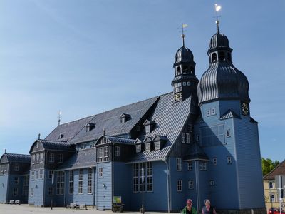 Das Bild zeigt eine blaue Holzkirche vor blauem Himmel. 