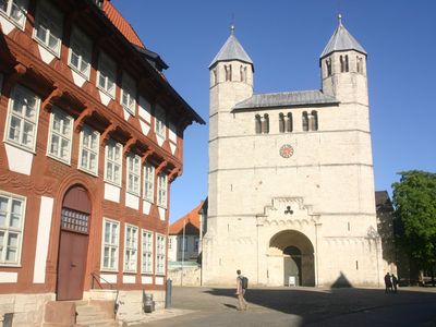 Das Bild zeigt ein historisches Fachwerkhaus und eine helle Kirche vor blauem Himmel. 