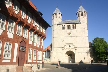 Das Bild zeigt ein historisches Fachwerkhaus und eine helle Kirche vor blauem Himmel. 