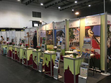 Messestand mit Roll-ups im Hintergrund. Im Vordergrund Counter in hellgrün mit weinroten Scherenschnitten im unteren Bereich.