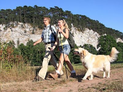 Das Bild zeigt einen Mann und eine Frau, die vor Klippen mit ihrem Golden Retriever wandern.