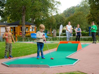 Das Bild zeigt spielende Kinder auf einer Minigolfbahn im Kurpark. 