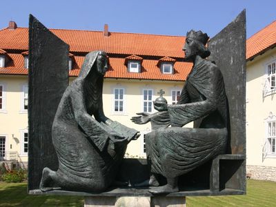 Das Bild zeigt den Roswitha-Brunnen, einen Brunnen mit zwei steinernen Statuen, die sich angucken.